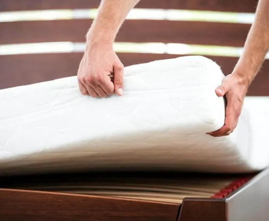 Person lifting a mattress on wooden bed frame.